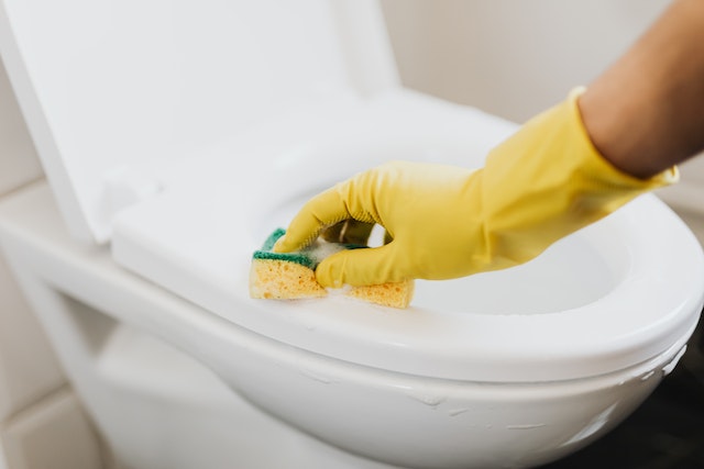 Cropped image of someone wearing yellow gloves using a sponge to deep clean a toilet